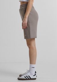 Brune bomullsshorts med elastisk midje og sidelommer, kombinert med hvite joggesko med svarte striper og sokker med logo.