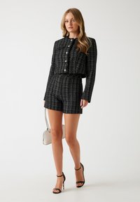 Zwart-witte geruite twee-delige set bestaande uit een cropped blazer met knopen en bijpassende high-waisted shorts. Glad textuur, aansluitend ontwerp.