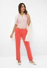 Gestreepte top met korte mouwen in wit en koraal, gecombineerd met koraalkleurige broeken en beige ballerina's. Een zacht, licht vest over de schouders geworpen.