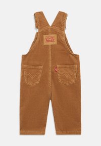 Overall de algodão estilo corduroy castanho com alças ajustáveis, bolso frontal e dois bolsos traseiros. Apresenta a costura e a etiqueta de logotipo características da Levi's.
