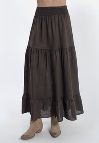 Lange bruine linnen rok met een smocktail, met tiered ruffles aan de onderkant, gecombineerd met lichtbruine cowboylaarzen.