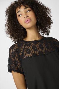 Black dress featuring a lace overlay on the shoulders and sleeves, with a smooth, solid fabric body and scalloped edges on the lace.