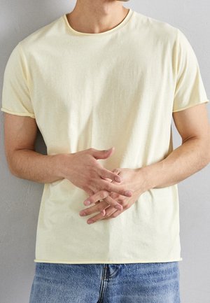 Hellgelbes Baumwoll-T-Shirt mit rundem Ausschnitt und kurzen Ärmeln, mit nahtlosem Abschluss und weicher Textur. Kombiniert mit Jeans.