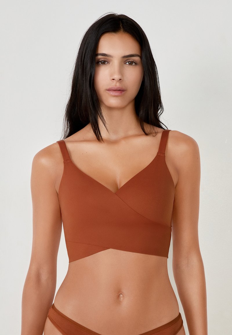 Bralette marrone senza cuciture con design a scollo a V, spalline regolabili e una texture liscia. Presenta una vestibilità aderente e uno stile minimalista.