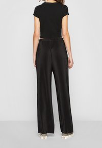 Svart kort t-shirt i kombination med vida, veckade svarta byxor. Byxorna har en slät textur och ett elastiskt midjeband.