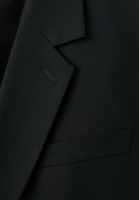 Blazer nero su misura con risvolto strutturato, tessuto elegante, taschino sul petto e dettagli di cucitura discreti.