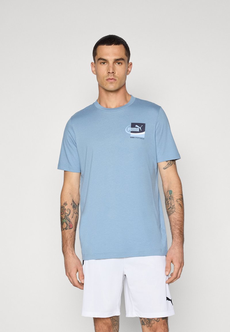 Tricou din bumbac de culoare albastru deschis, cu mâneci scurte, gât rotund și un mic logo Puma pe piept. Purtați cu pantaloni scurți albi.