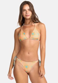 Trojuholníkový bikini v pastelovej oranžovej farbe s kruhovými vzormi. Uväzovanie na stranách, textúrovaná tkanina, nastaviteľné ramienka a podložené košíky.