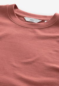 Lässiges T-Shirt aus weichem, staubigem Rosé-Baumwollstoff. Es hat einen klassischen Rundhalsausschnitt und eine glatte Textur mit minimalen Nähdetails.