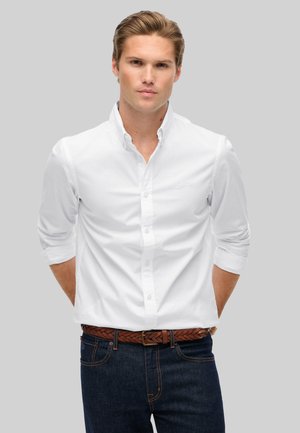 Witte overhemd met lange mouwen, opgekruld bij de manchetten. Draag het met een donkere denim jeans en een gevlochten bruine leren riem. Duidelijke, gladde stof textuur.