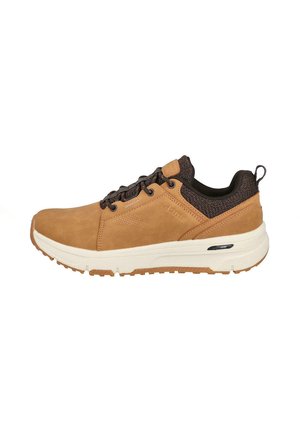 Deportivo de ante marrón con acentos de malla negra, entresuela blanca y suela de goma texturizada. Presenta un diseño con cordones y un bucle en la parte posterior.
