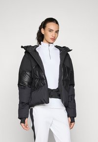 Schwarze Daunenjacke aus einer Mischung aus glänzenden und matten Texturen. Verfügt über eine Kapuze, einen Reißverschluss vorne und elastische Bündchen; gestylt mit einem hochgeschlossenen Oberteil.