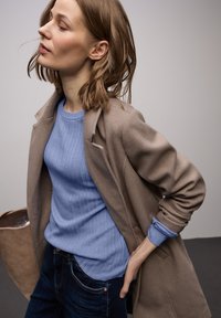 Cappotto marrone chiaro sopra un maglione azzurro chiaro a coste. Jeans scuri con una texture sottile. Design semplice, hardware minimo e colori neutri.