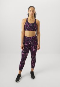 Juodos spalvos sportinis liemenukas ir leggingai su rožinėmis gėlių detalėmis. Medžiaga atrodo tampri, o dizainas prigludęs. Juodi sportiniai bateliai papildo ansamblį.