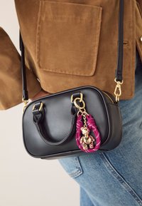 Zwarte leren tas met goudkleurige hardware, dubbele bovenhandvatten en een afneembare fuchsiakleurige riem met een gouden teddybeerbedel.