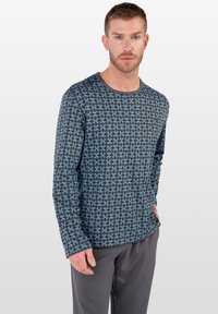 Langärmliges Hemd im blauen und schwarzen Wirbelmuster, aus weichem Stoff. Rundhalsausschnitt und enganliegende Ärmel, kombiniert mit grauen Hosen.