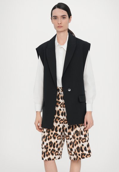 Black sleeveless blazer with a single button, paired with beige and black leopard print shorts. Model in a white shirt underneath.