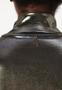 Fényes fekete anyag, fémes csillogással, gallérral és a hátsó részén egy kis fémes fakkal, amely szalag formájú.