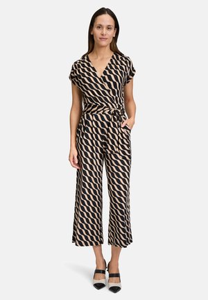 Black and beige patterned jumpsuit with a V-neck, short sleeves, a tied waist, and wide-leg trousers. Worn with two-tone heels.