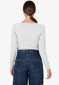 Grijze longsleeve shirt met een ronde hals, gecombineerd met hoge, versleten donkerdenim cargo broeken met zakken.