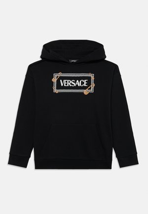 Sudadera con capucha negra que presenta un logotipo central en blanco de "VERSACE" contorneado con un patrón a cuadros y adornado con alfileres de seguridad dorados.