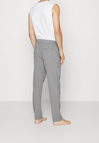 Šedé volně střižené tepláky s elastickým pasem a jedním zadním kapsou, spojené s bílým tílkem bez rukávů. Bosý.