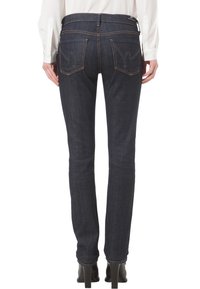 Ciemnoniebieskie dżinsy o slim fit, z kontrastującymi przeszyciami i dwoma tylnymi kieszeniami, noszone z białą bluzką z długim rękawem.