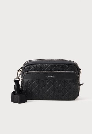 Schwarze Calvin Klein Umhängetasche mit eingeprägtem geometrischem Muster, Vordertasche mit Reißverschluss, silbernem Reißverschluss und verstellbarem Stoffriemen.