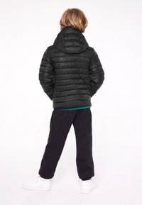 Czarna kurtka puchowa z pikowaną fakturą i kapturem, noszona na turkusowej koszuli. Do tego czarne spodnie i białe trampki.