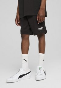 Shorts en coton noirs avec le logo Puma blanc, associés à des baskets blanches avec des accents noirs et des chaussettes blanches avec un petit logo Puma noir.