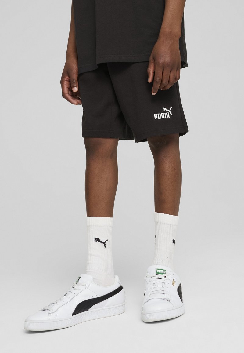 Shorts en coton noirs avec le logo Puma blanc, associés à des baskets blanches avec des accents noirs et des chaussettes blanches avec un petit logo Puma noir.