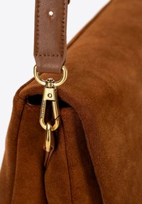 Hoek van een bruine leren handtas, met een goudkleurige metalen sluiting en een bruine leren schouderriem met stikseldetails. Gladde textuur, eenvoudig ontwerp.