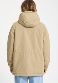 Beige insulated jacket with a hood, elastic cuffs, and a slightly loose fit. Simple design, no visible logos or patterns, smooth texture.
