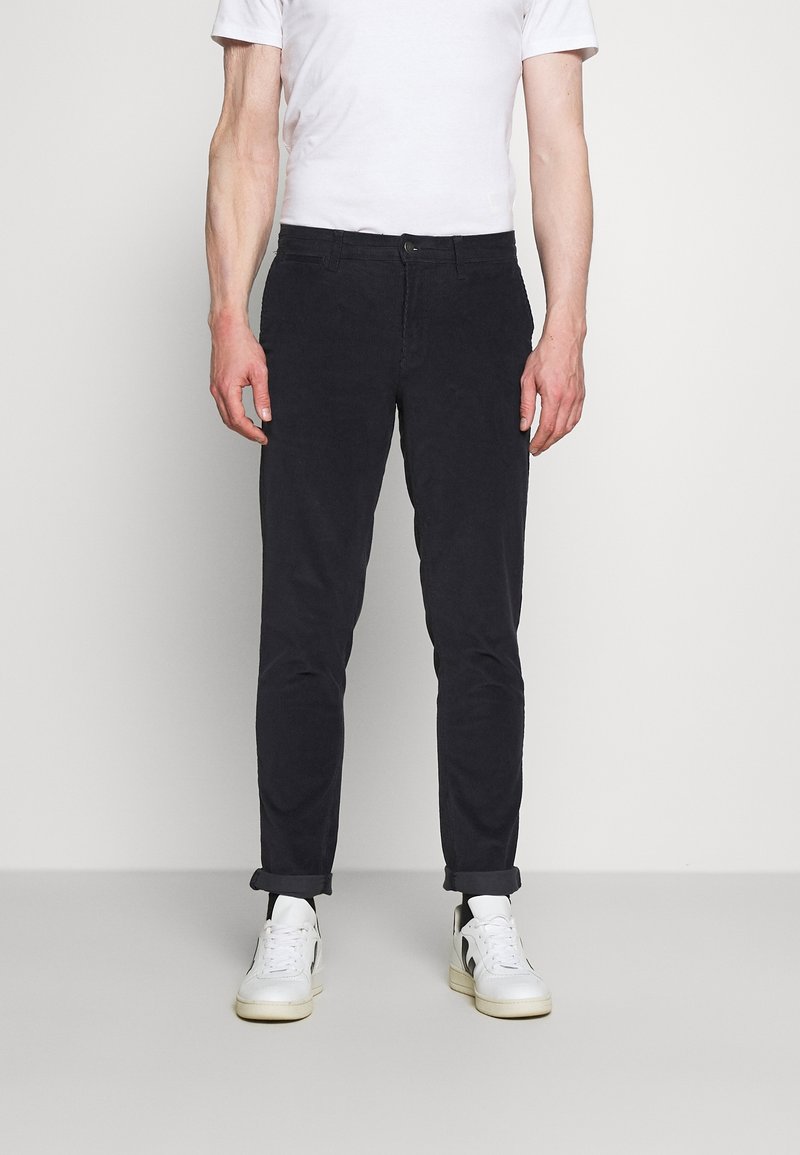 Tmavě námořnické slim-fit kalhoty s jemnou texturou, zapínáním na knoflík a ohrnutými nohavicemi, spárované s bílými teniskami.