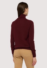 Burgundský rolák s přiléhavým střihem a žebrovanými manžetami, doplněný béžovými kalhotami. Hladký materiál, minimální detaily.