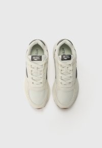 Light-colored sneakers with mesh and suede materials, featuring gray accents and a rubber sole, laced design, and labeled tongue.