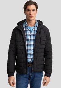 Giubbotto puffo nero con cappuccio e polsini elastici, con zip frontale e tasche laterali, indossato sopra una camicia a quadri blu e bianchi.