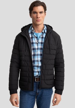 Giubbotto puffo nero con cappuccio e polsini elastici, con zip frontale e tasche laterali, indossato sopra una camicia a quadri blu e bianchi.