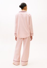 Set de pijama roz deschis dintr-un material moale, care include o cămașă cu nasturi, guler și mâneci lungi, alături de pantaloni larga cu detalii contrastante.