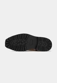 Semelle en caoutchouc avec des rainures profondes, offrant une traction. Dessus en cuir beige avec une finition lisse, présentant un design à bout arrondi et des accents de couture minimalistes.