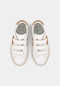 Hvite sneakers med tre borrelåser, brune gummidetaljer og en teksturert såle. Har en grå innersåle med logo. Glatt skinnutside.