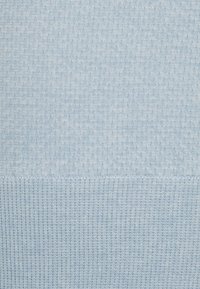 Helles blaues gestricktes Material mit einem strukturierten Muster, das am unteren Rand eine gerippte Kante für zusätzliche Struktur und Detail aufweist.