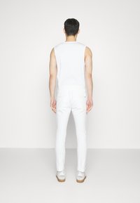 Witte mouwloze top, witte nauwsluitende broek en lichtgekleurde sneakers. Eenvoudig ontwerp, gladde textuur en neutraal kleurenschema.