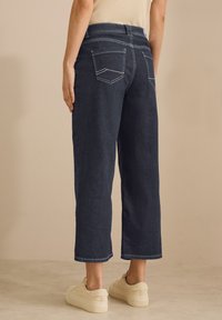 Los pantalones vaqueros de tiro alto, color azul oscuro y de pierna ancha, presentan dos bolsillos traseros con costuras en contraste y un corte recto hasta el tobillo.
