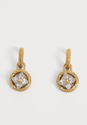 Boucles d'oreilles créoles en or avec pendentifs ronds comportant quatre pierres précieuses transparentes en forme de cœur formant une fleur, entourées de petits cristaux et gravure du nom de la marque.