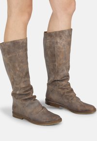 Bottes en cuir marron à l'aspect décontracté, avec une texture douce, de conception mi-mollet et semelles plates. Présentent des coutures visibles et une finition subtilement usée.