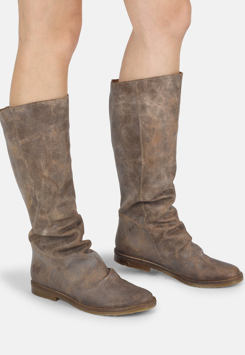 Botas de cuero marrón tipo slouch con una textura suave, diseño hasta la rodilla y suelas planas. Presentan costuras visibles y un sutil acabado desgastado.