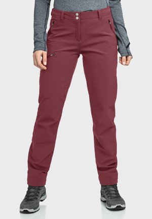 Woman wearing burgundy hiking pants with zip pockets and gray hiking boots, standing with hands relaxed at sides.