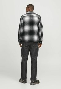 Black and white plaid overshirt with a button collar, long sleeves, and a loose fit, paired with dark jeans and black sneakers.