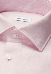 Chemise en lin rose clair avec boutons blancs et une étiquette de marque "seidensticker" visible à l'intérieur du col.